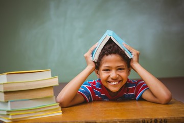 Little boy holding book over head in classroom