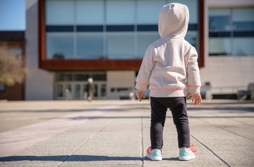 Little girl with sneakers and hoodie standing outdoors
