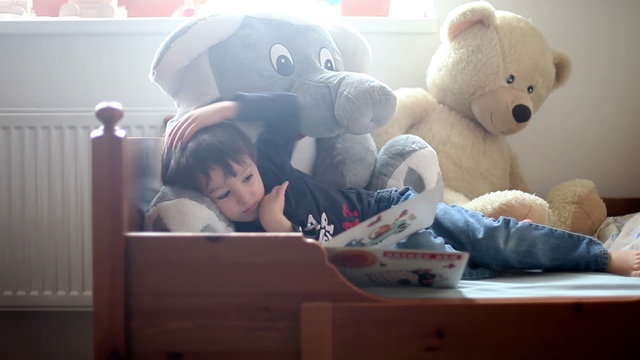 Cute boy, reading a book in bed, fluffy toys around him