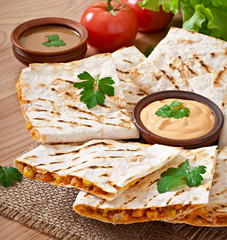 Mexican Quesadilla sliced with vegetables and sauces on the tabl