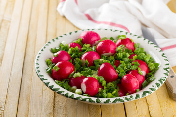 Bowl of red radishes and green onions on a wooden background