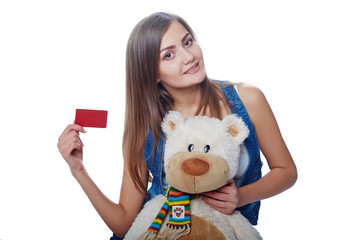 Young cheerful girl holding big soft toy bear and card of the ba