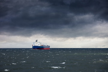 Dark cloudy stormy sky with ship and waves in the sea.
