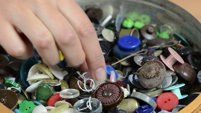 Dish of various colorful buttons and needlewoman finger choose