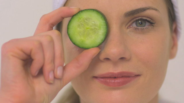 BCU OF A WOMAN HOLDING A CUCUMBER SLICE HER OVER EYE