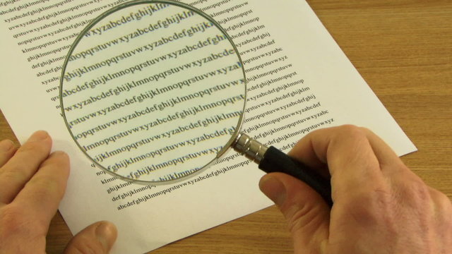 Male picking up Magnifying Glass to look at small print in contract