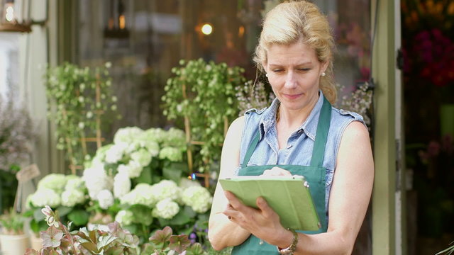 A Florist stands in the doorway of her shop typing into her digital tablet