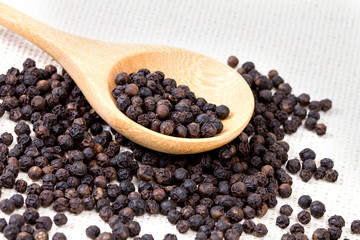 closeup black pepper in wooden spoon on fabric