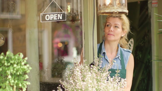 A Florist walks up to the entrance of her shop and flips the sign to open, beginning a day of successful business