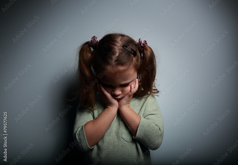 Wall mural Crying kid girl holding face the hands and looking down