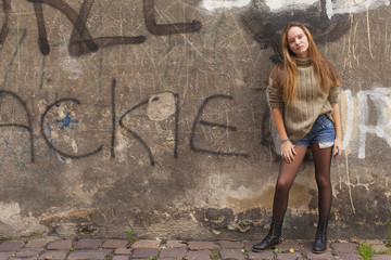 Girl in shorts and sweater standing near the wall in old city.
