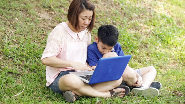 Happy asian mother and child playing laptop in garden .