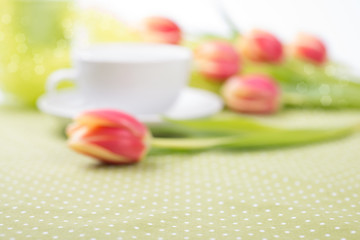 Burred background with red tulips on the table and tea cup out o