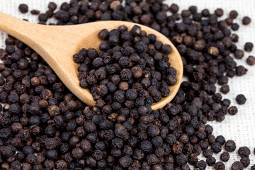 closeup black pepper in wooden spoon on fabric