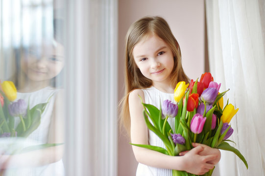 Adorable little girl holding tulips by the window