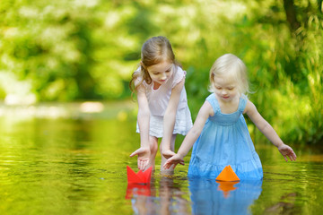 Two sisters playing with paper boats by a river