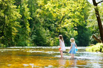 Two sisters playing with paper boats by a river