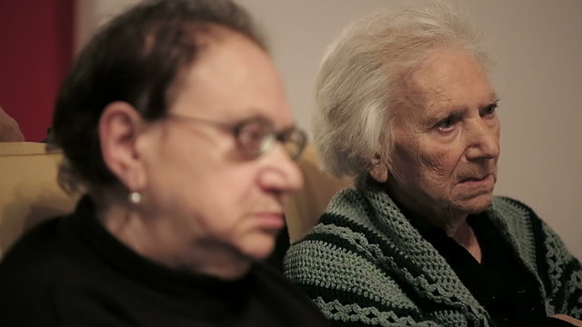 Two seniors women watching tv at home on couch