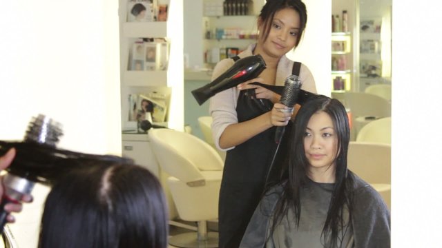 MS, Hairdresser drying and brushing hair of female in hair salon