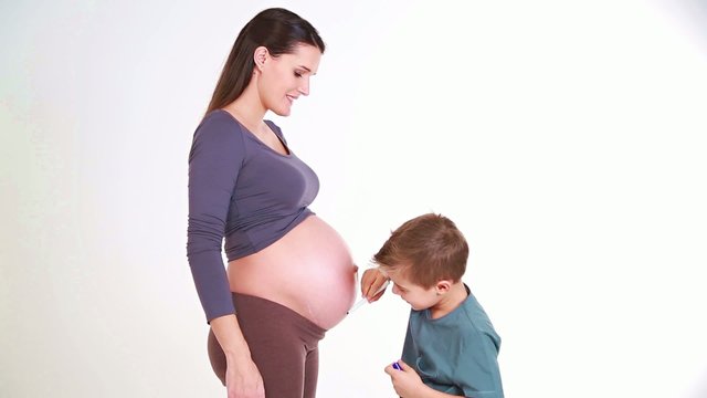 young boy draws hearts and kisses the belly of his mother