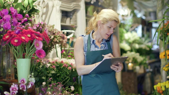 A Florist speaks on the phone, inspecting the supplies in her shop and noting it on her clipboard