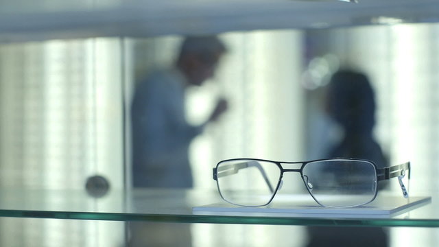 Female Optician guides and asssits Male patient to choose a new pair of glasses