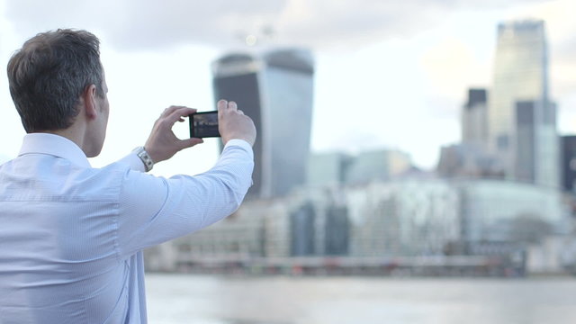 Business man takes a photo of the city scape and River Thames with his smart phone