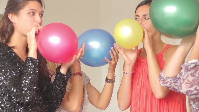 Females friends blowing up balloons at party