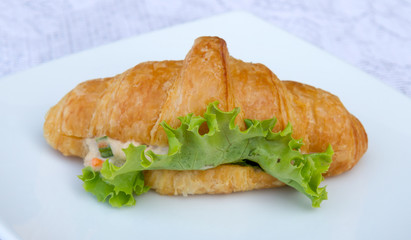 Sandwich croissant with vegetable on white plate.