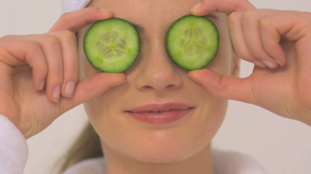 BCU OF A WOMAN HOLDING CUCUMBER OVER HER EYES
