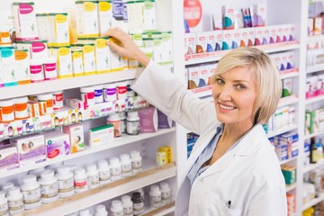 Smiling pharmacist taking box from shelf