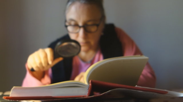 senior lady reading a book with a magnifier