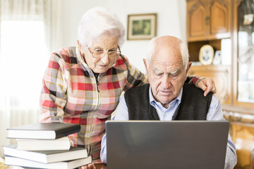 Fototapeta premium Senior couple looking for information in books and internet