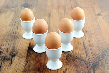 five egg cups with natural brown eggs in arrow shape on table