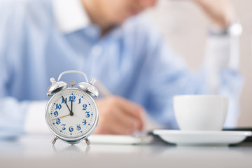 Man working in office. Focus on clock in foreground. 