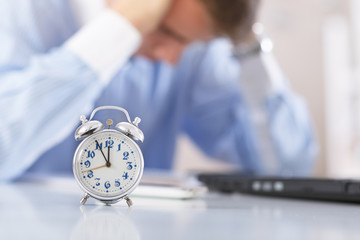 Man working in office. Focus on clock in foreground. 