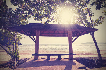 Retro filtered photo of a covered seaside bench at sunset.