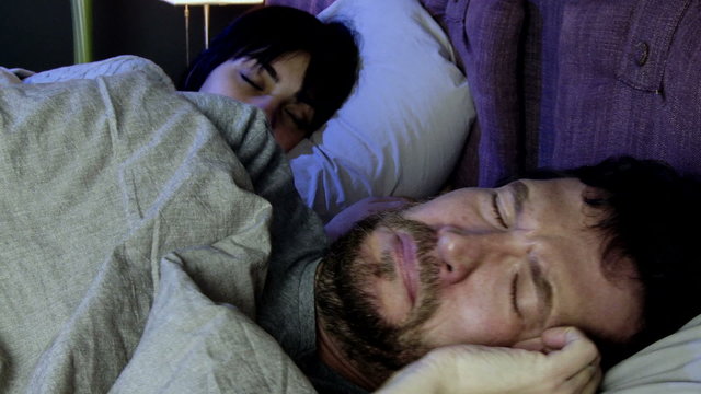 Man crying in bed with sleeping girlfriend