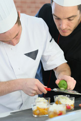 Young cook preparing dessert with chef behind him