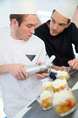 Young cook preparing dessert with chef behind him