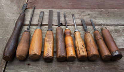 Old vintage carpenter chisels and tools laying on wooden table in a row.