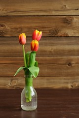 Red and yellow tulips in glass bottle on wooden background