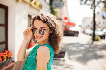 Woman in round sunglasses smiling over shoulder in city street