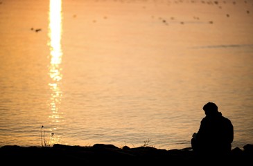 silhouetted man sitting at lake in sunset light