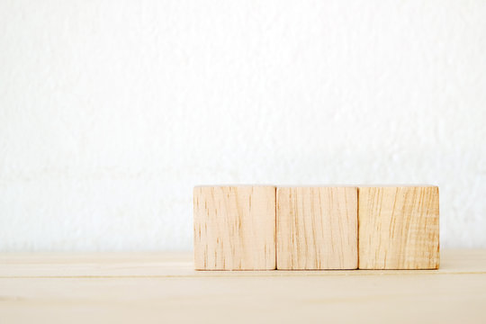 Three wooden cubes on table over white wall background