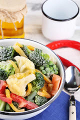 Frozen vegetables in bowl on napkin, on wooden table background