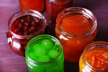 Homemade jars of fruits jam on color wooden background
