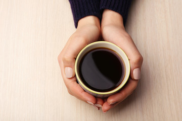 Female hands holding cup of coffee on wooden background