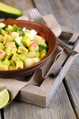 Salad with apple and avocado in bowl on tray on table close up