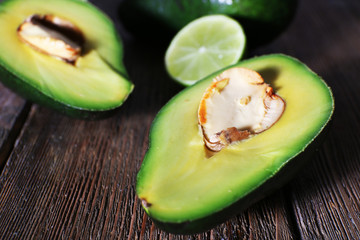Sliced avocado with pieces of lime on wooden background